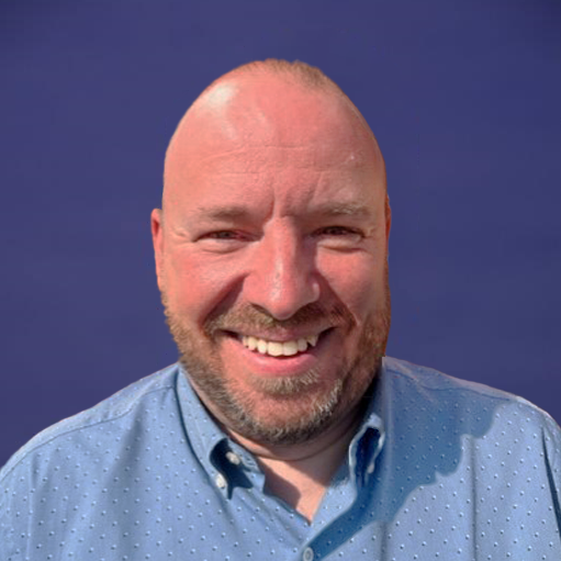 A bald man with a beard is smiling in front of a blue background.