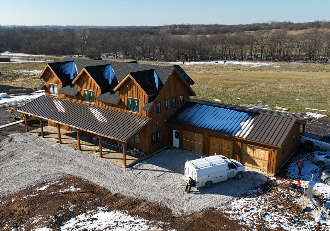 Brown wooden barn-style building with a covered porch and snowy landscape. A white van is parked nearby.