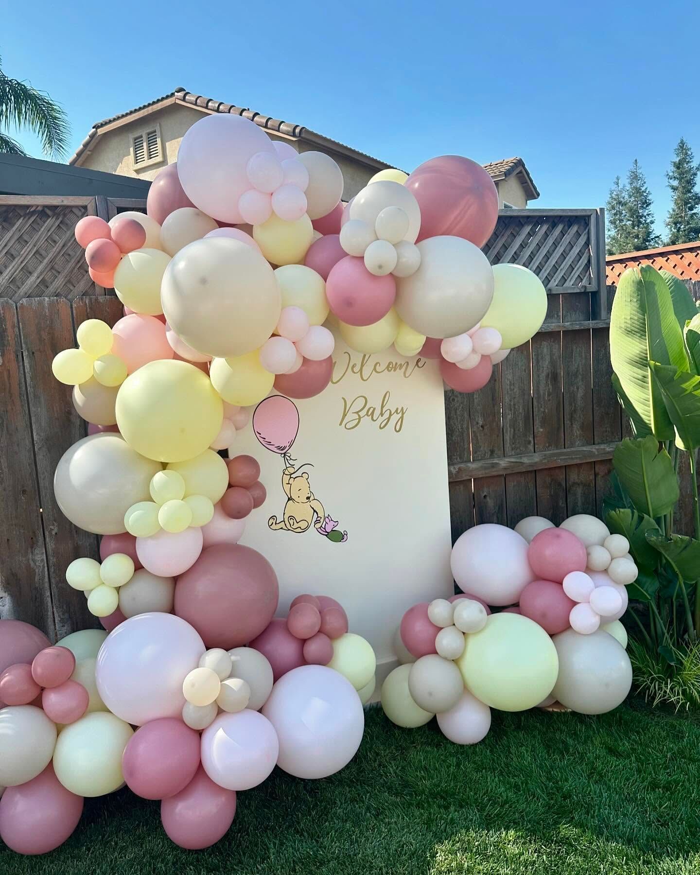 Baby shower decor with balloon garland in pastels: pink, yellow, cream. Sign says