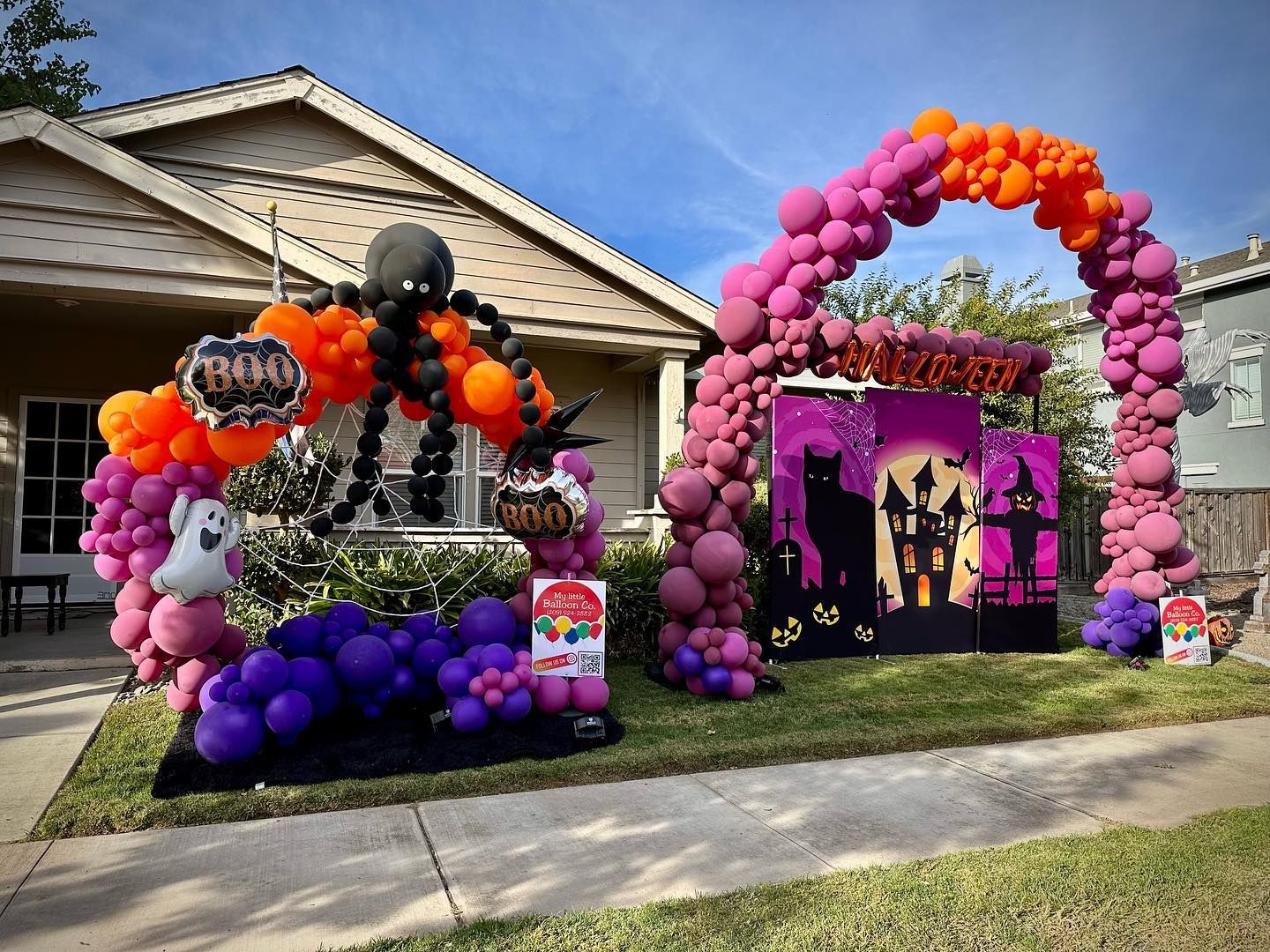 Halloween decorations with balloon arches, a haunted house, and spider, in front of a house.