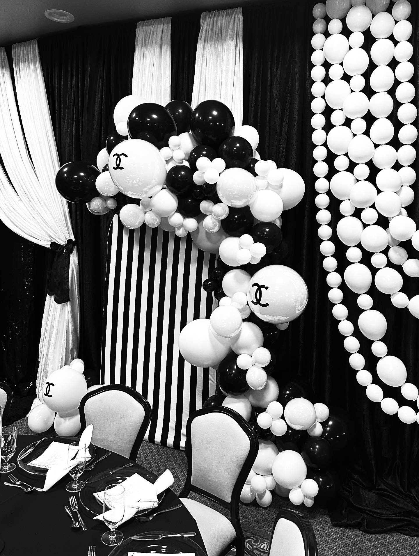 Black and white balloon arch with Chanel logo, against a striped backdrop and chairs.