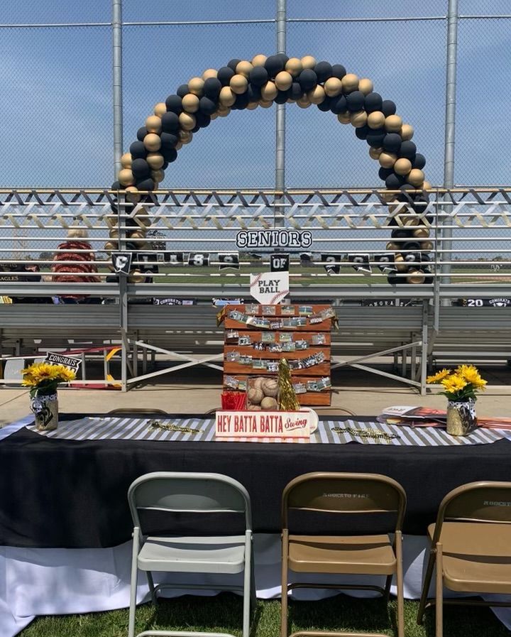Baseball-themed graduation celebration with black and gold balloon arch and table display.