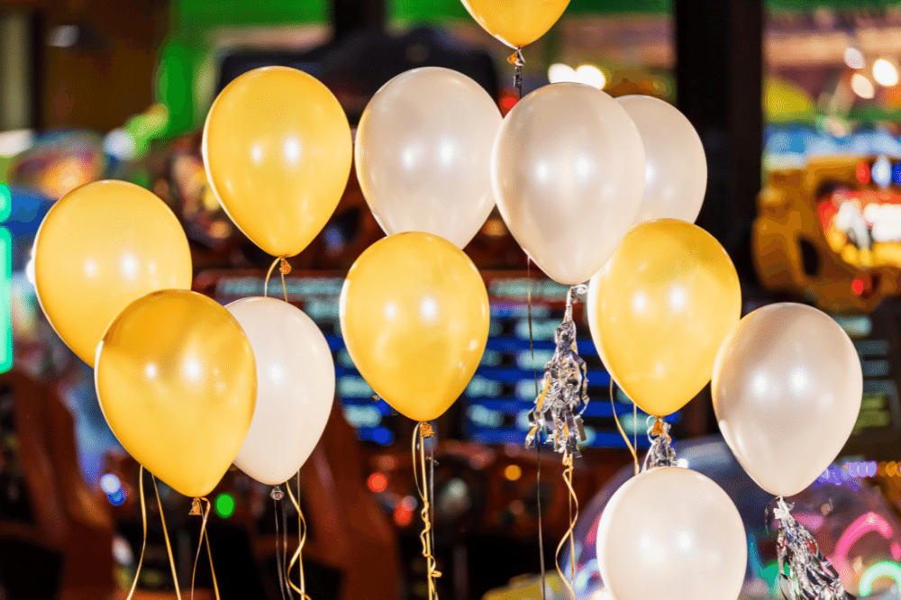 Gold and white balloons floating in front of an arcade with colorful lights.