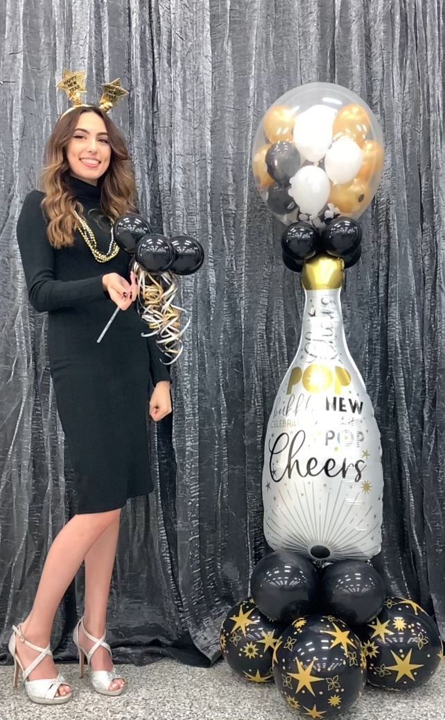 Woman in black dress with champagne balloon arch.