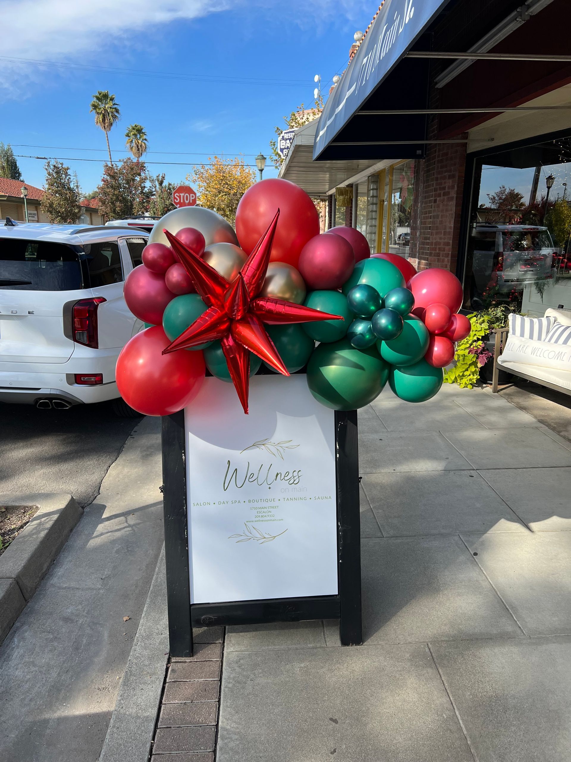 A-frame sign with Christmas balloon display, red, green, gold, and silver balloons, and a red star.