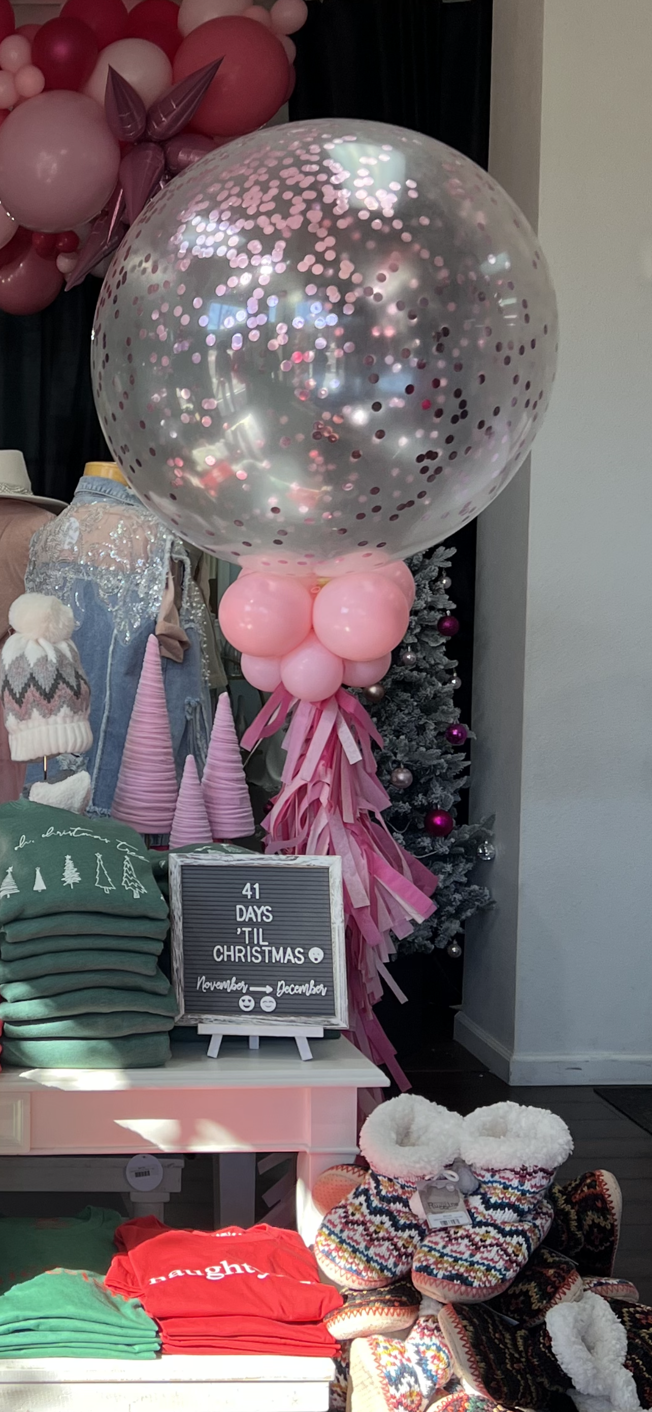 Storefront display with a large clear balloon with confetti, other pink balloons, and merchandise.