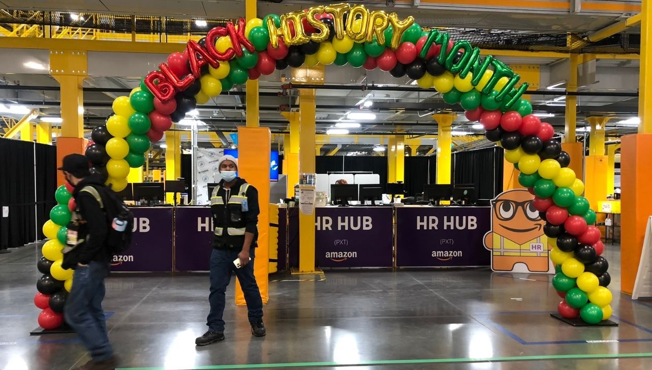 People walking through a balloon arch in red, black, yellow, and green that says 