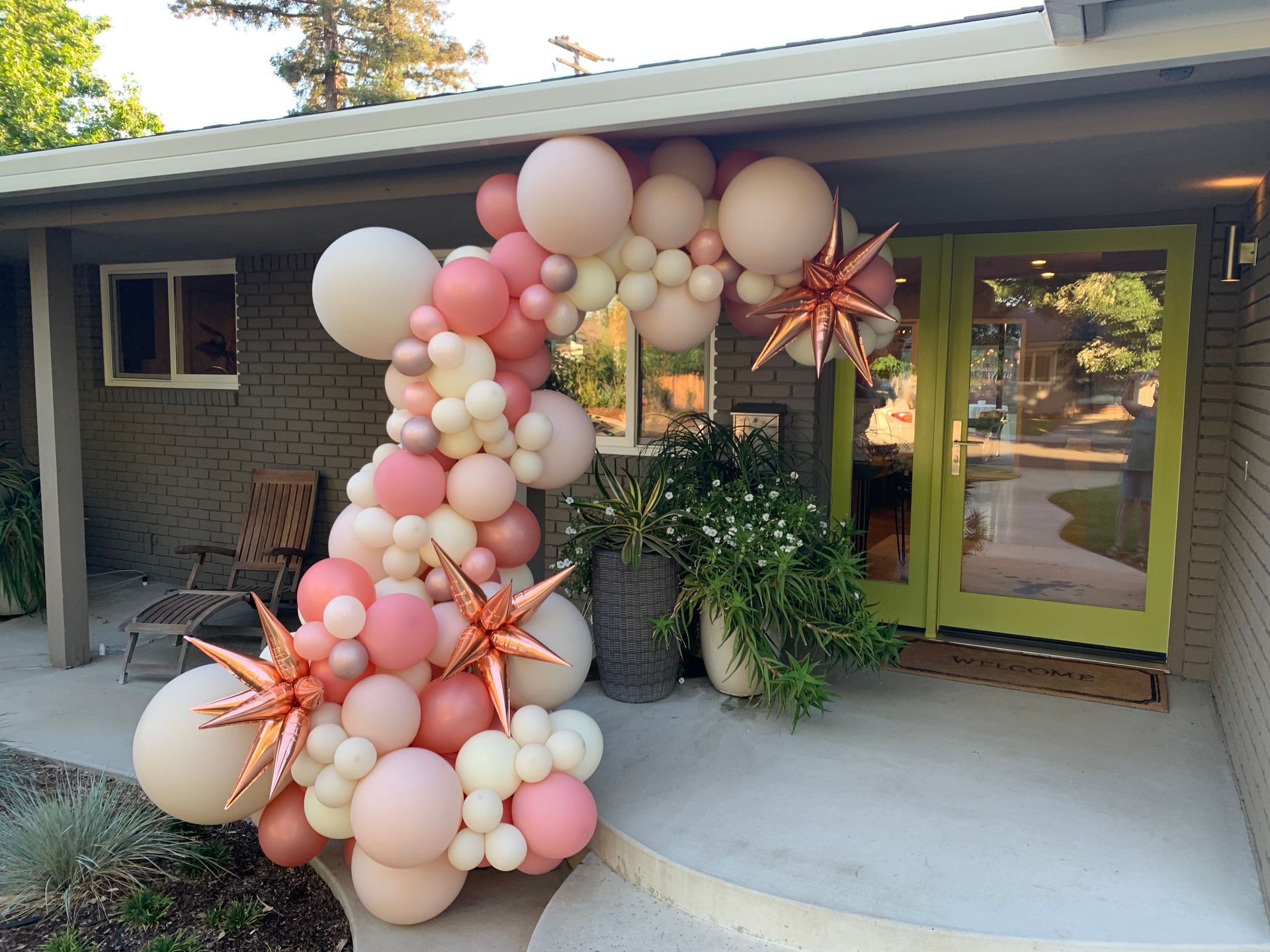 Balloon arch in shades of pink and white, with star accents, decorating a home's entrance.