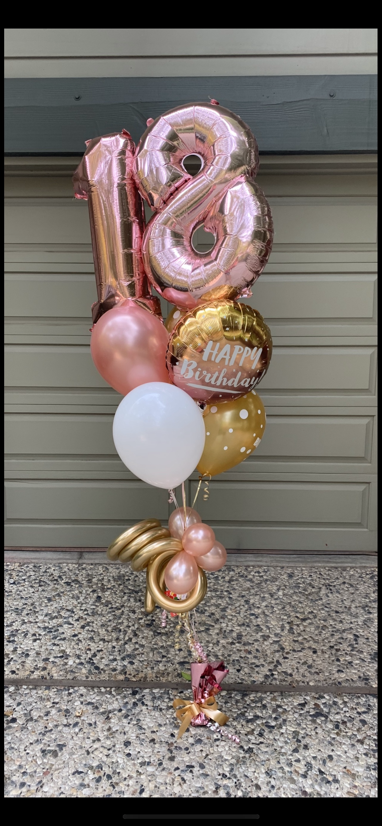 Balloons shaped as “18”, and other balloons, rose gold, white, and gold, on a stone surface.