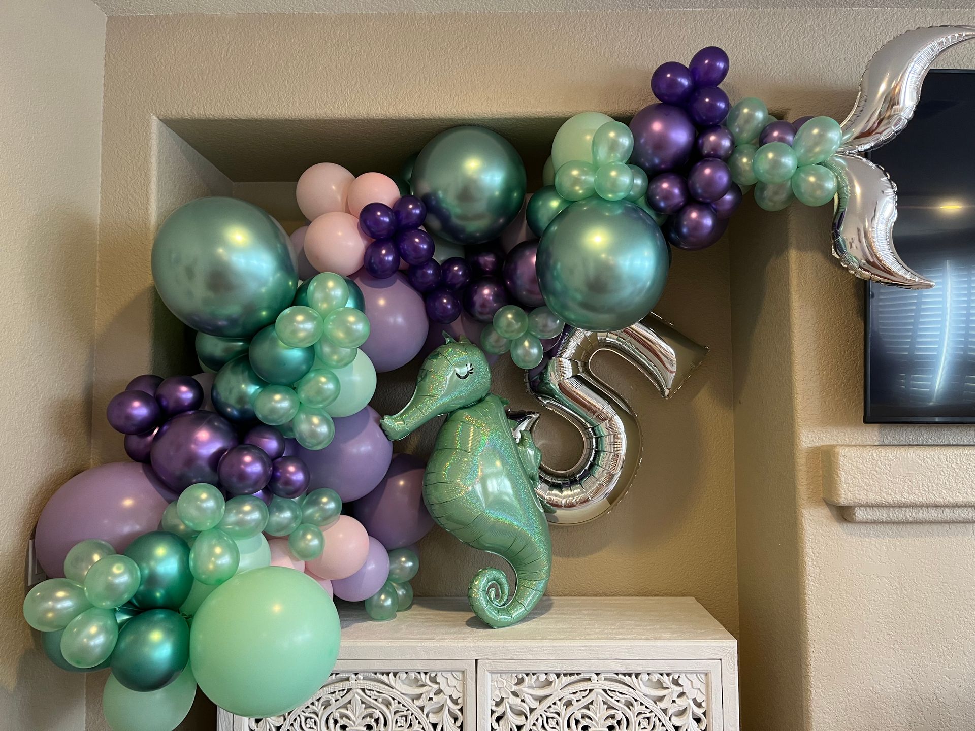 Mermaid-themed balloon garland with teal, purple, and pink balloons, a seahorse and a silver 