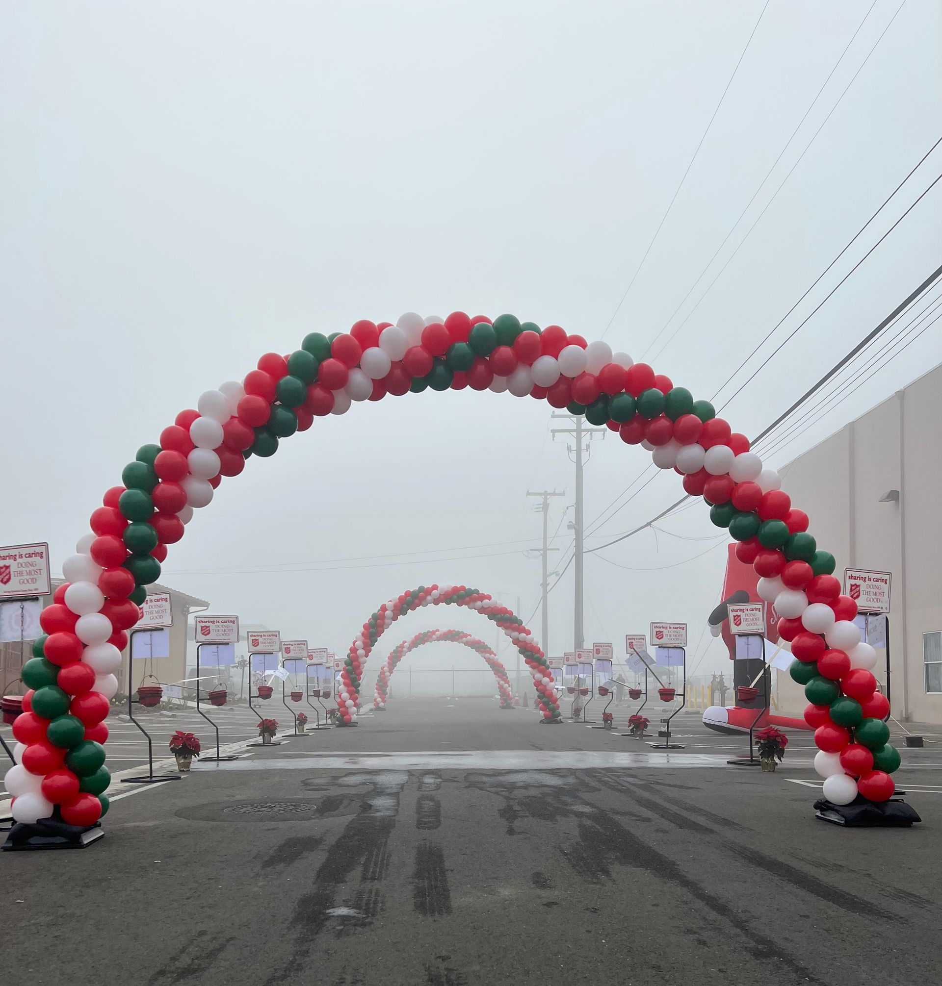 Three balloon arches, red, white, and green, line a road in foggy conditions.