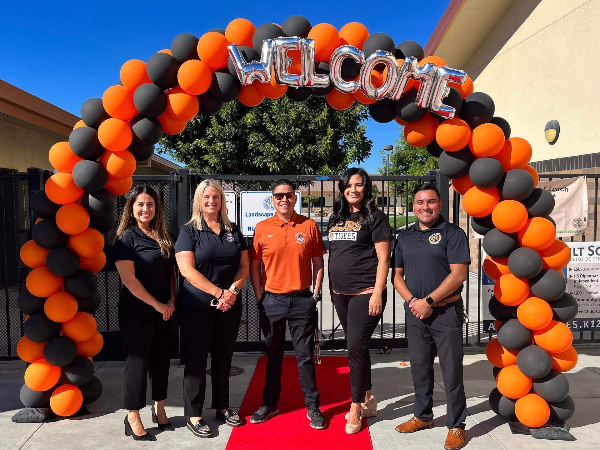 Five people stand under a balloon arch that says 