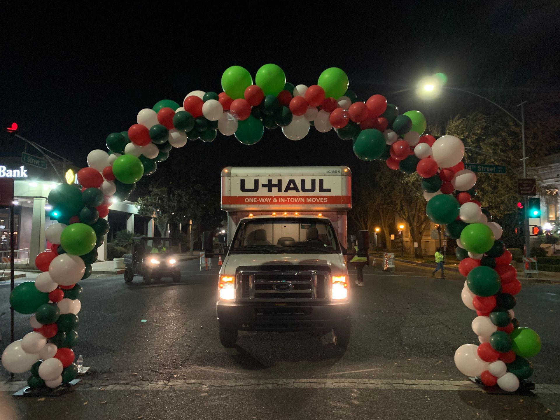 U-Haul truck driving through a balloon archway with red, white, and green balloons at night.