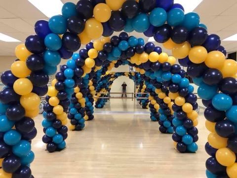 Rows of balloon arches in yellow, blue, and navy, forming a colorful tunnel in a room.