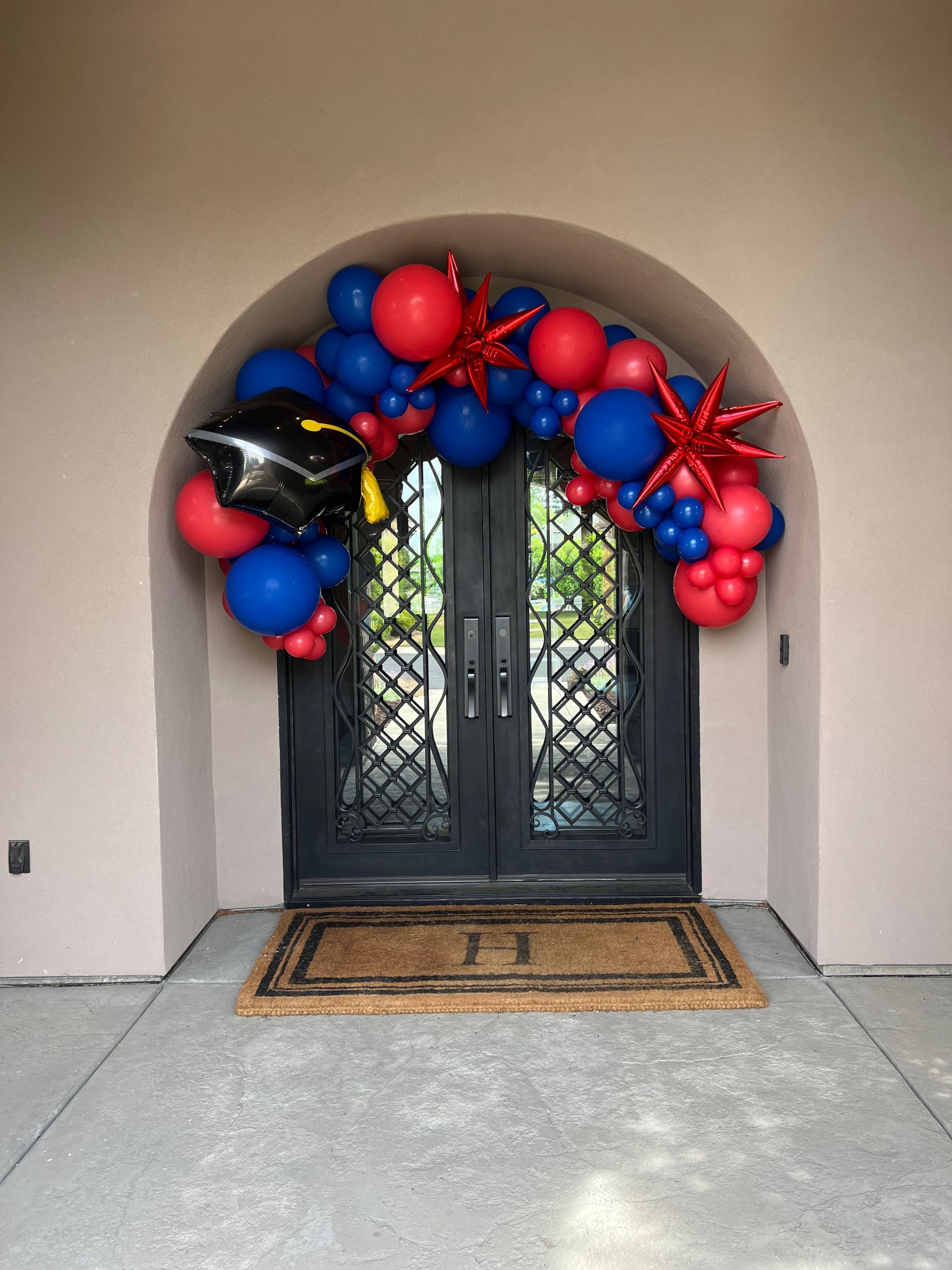 Graduation arch with red, blue balloons, starbursts, and cap over a doorway.