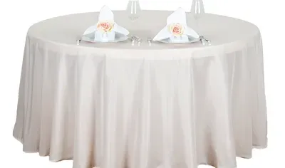 A round, cream-colored table set for a formal occasion; two place settings with napkins and floral accents.