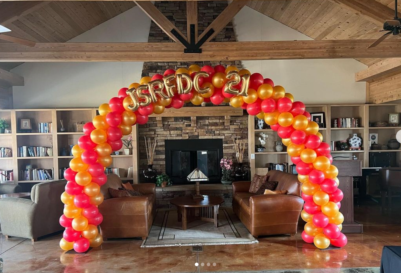 Arch of red and orange balloons; gold letters spell 