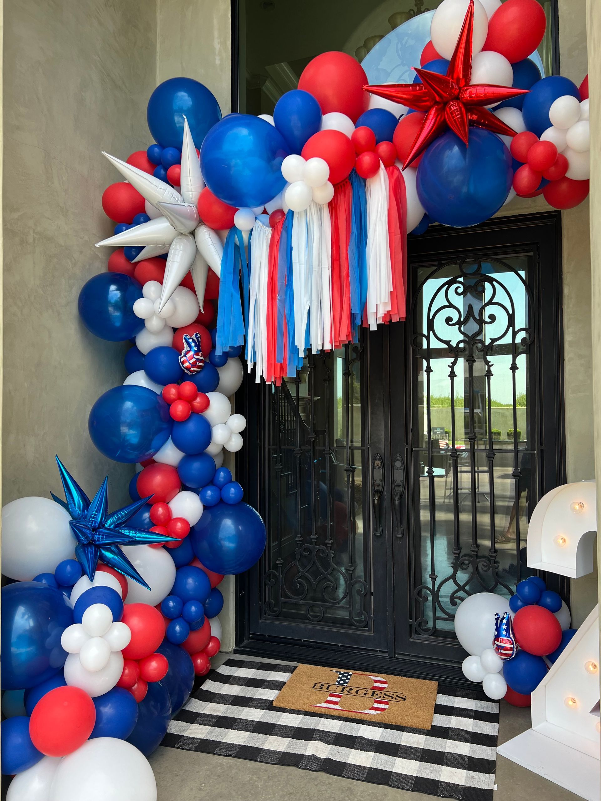 Festive Fourth of July entryway decorated with red, white, and blue balloon arch, star accents, and door.