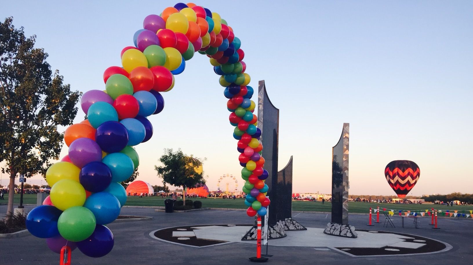 A rainbow balloon arch over a memorial with a hot air balloon in the sky.