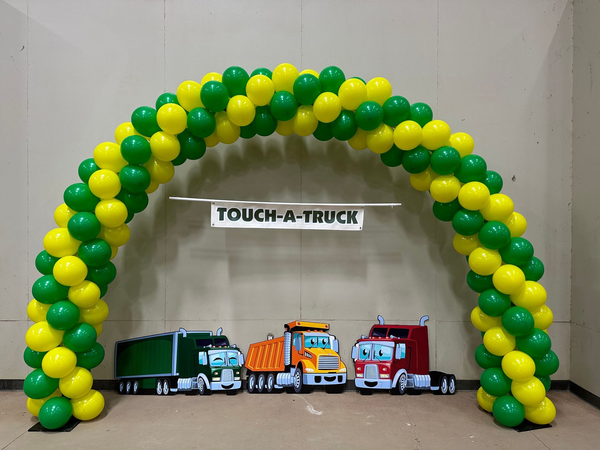 A balloon archway in green and yellow over toy trucks at a 