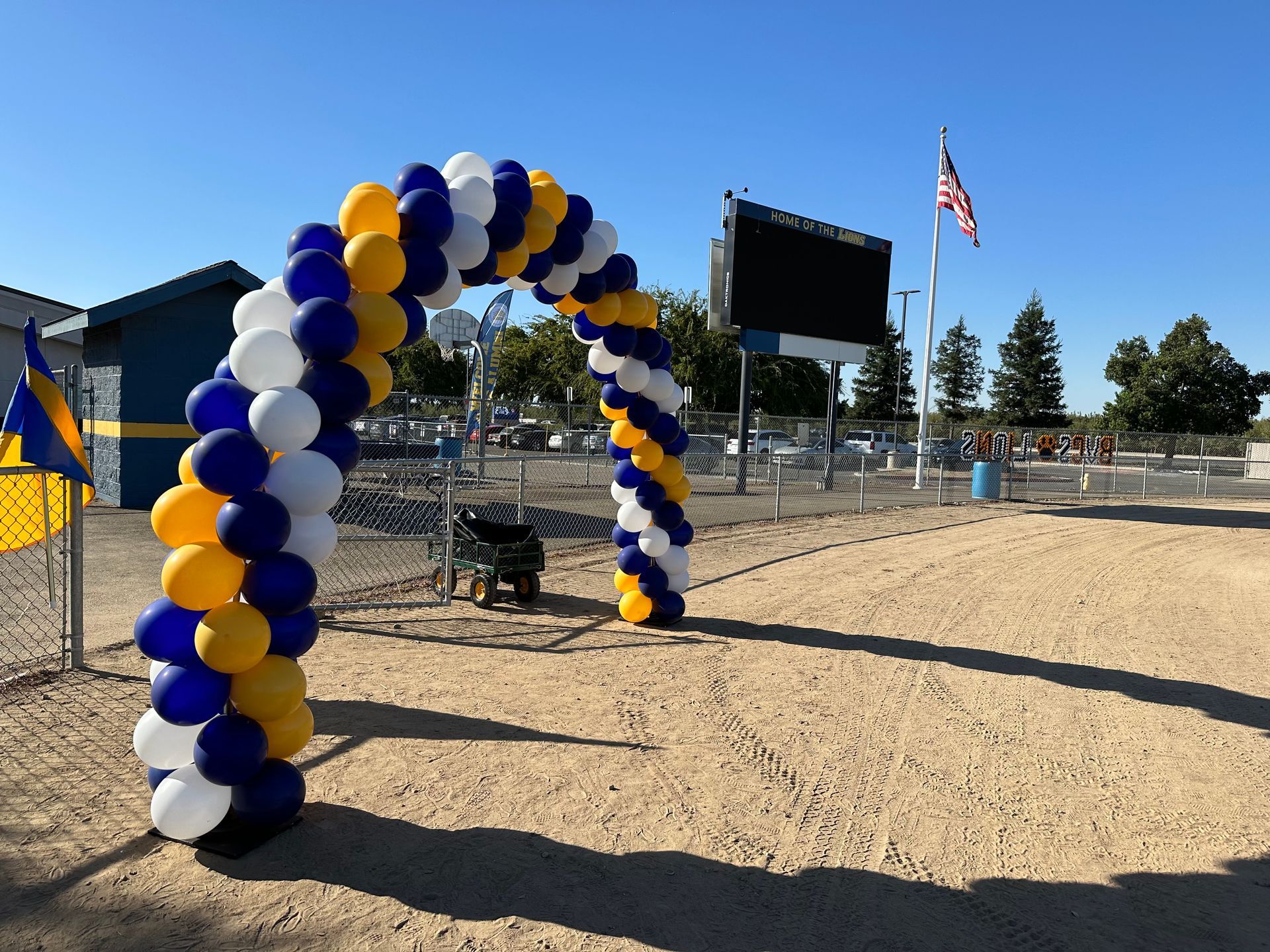 Balloon archway in blue, white, and gold, framing an entrance to a venue with an American flag.