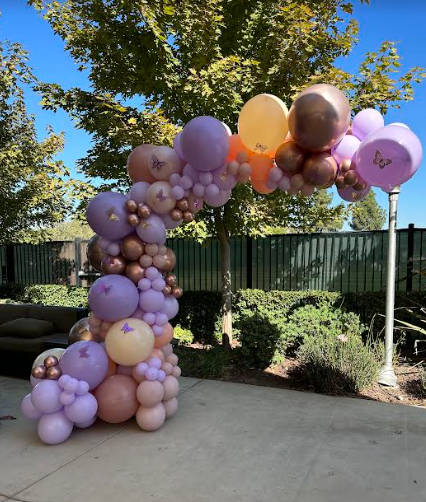 Balloon arch in shades of pink, purple, and gold, set outside.