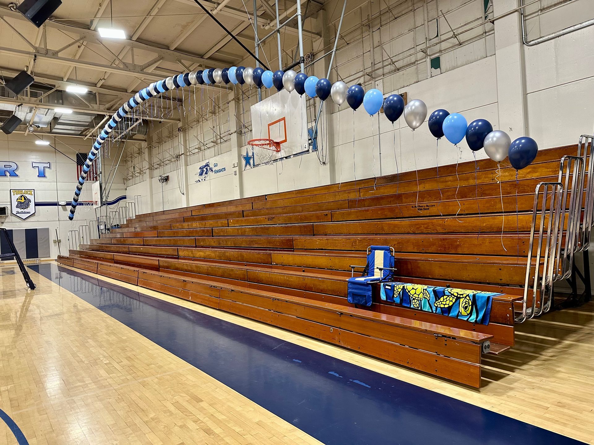 Gymnasium with wooden bleachers, a balloon arch, and a small setup for an event.