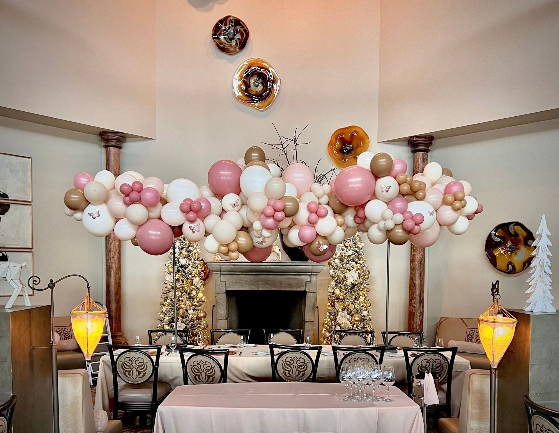 Elegant dining room decorated with a balloon garland in pink and gold, over a long table set for a gathering.