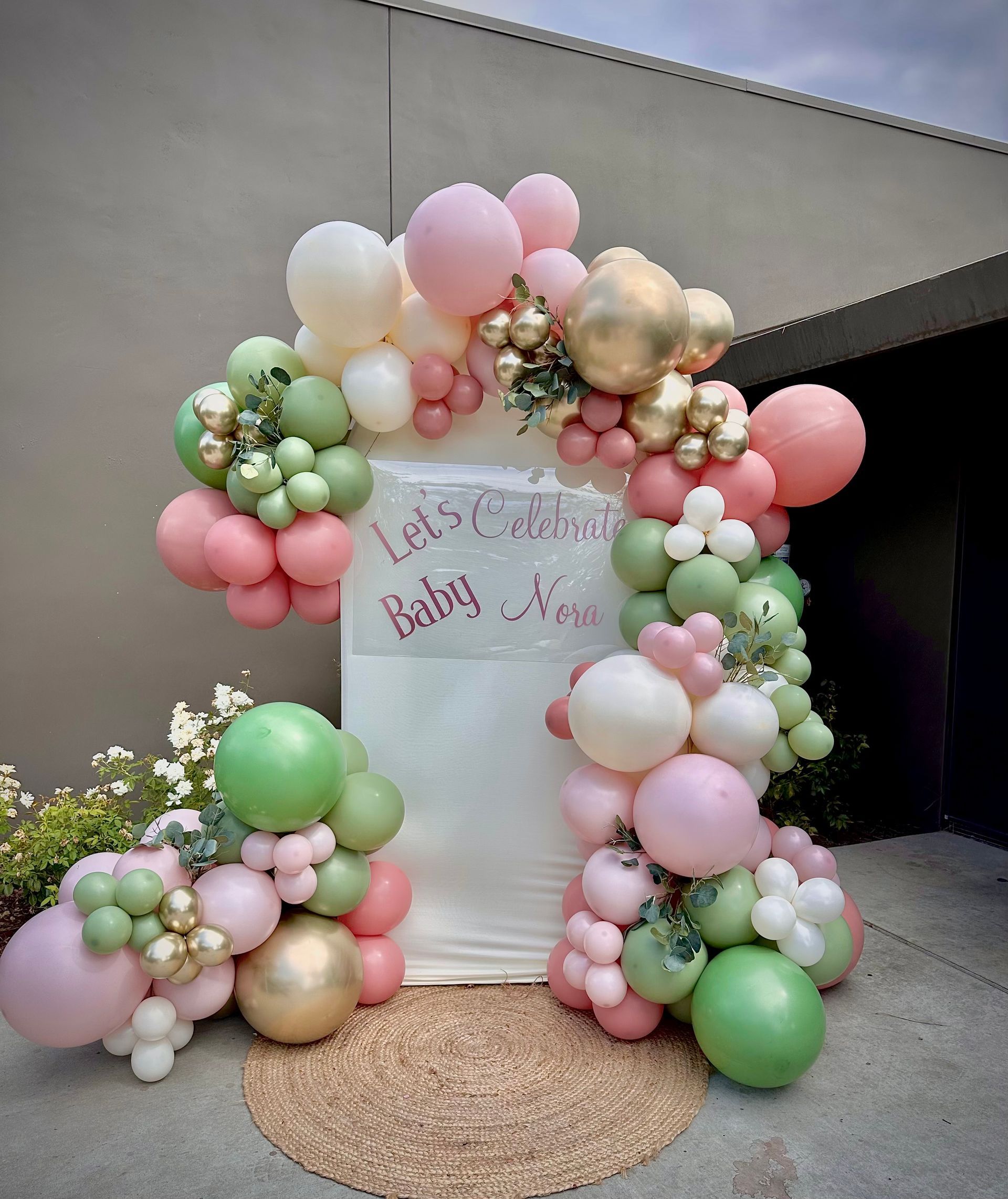 Balloon archway for a baby shower with pink, green, and gold balloons, with a sign that says
