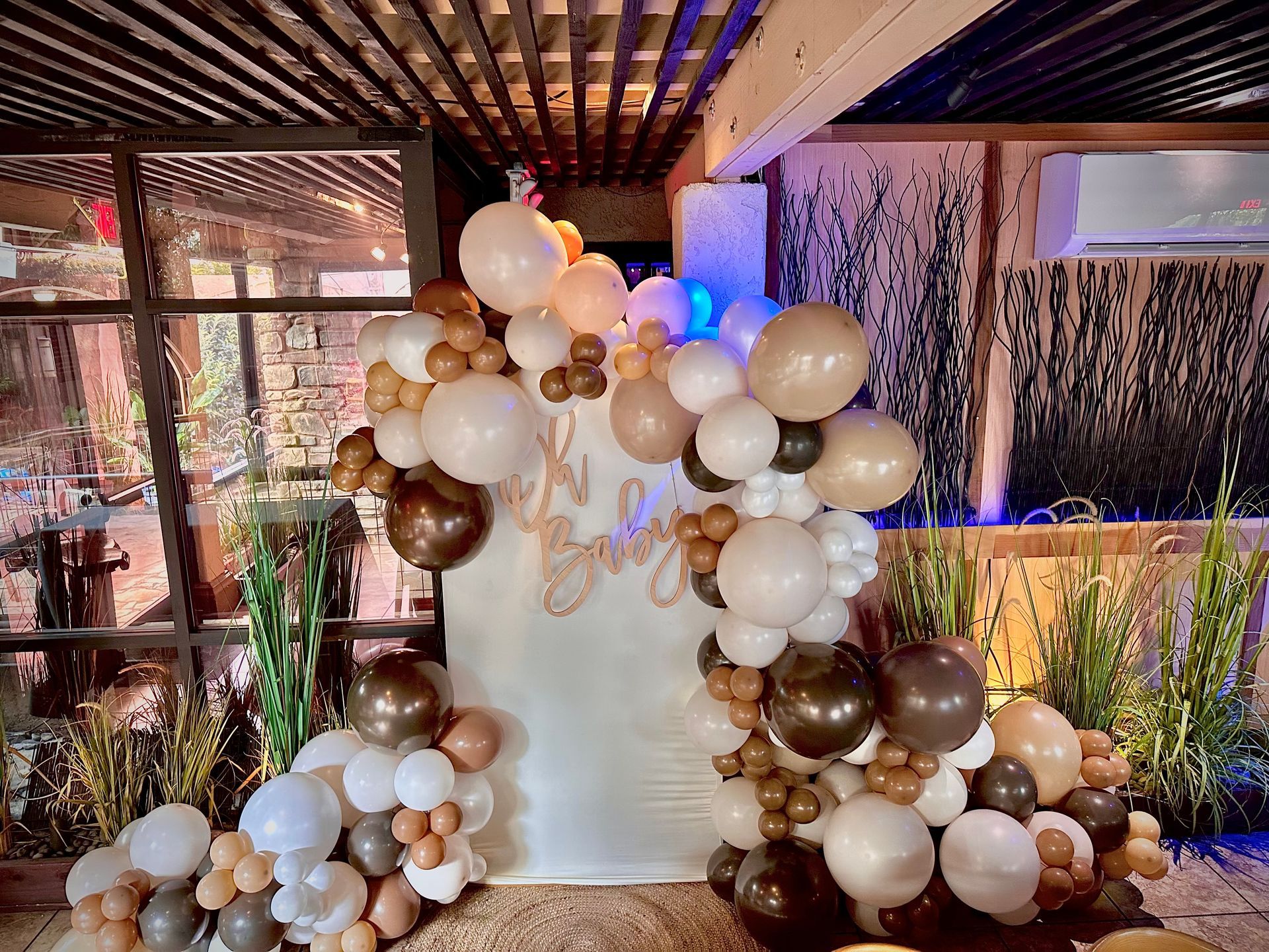 A backdrop with a balloon arch in brown and white, celebrating a baby shower.