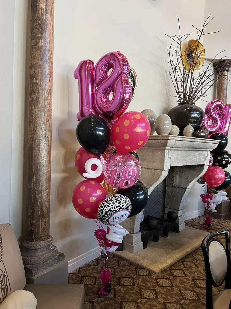 Pink and black 18th birthday balloon bouquet with polka dots, next to a pillar and fireplace.
