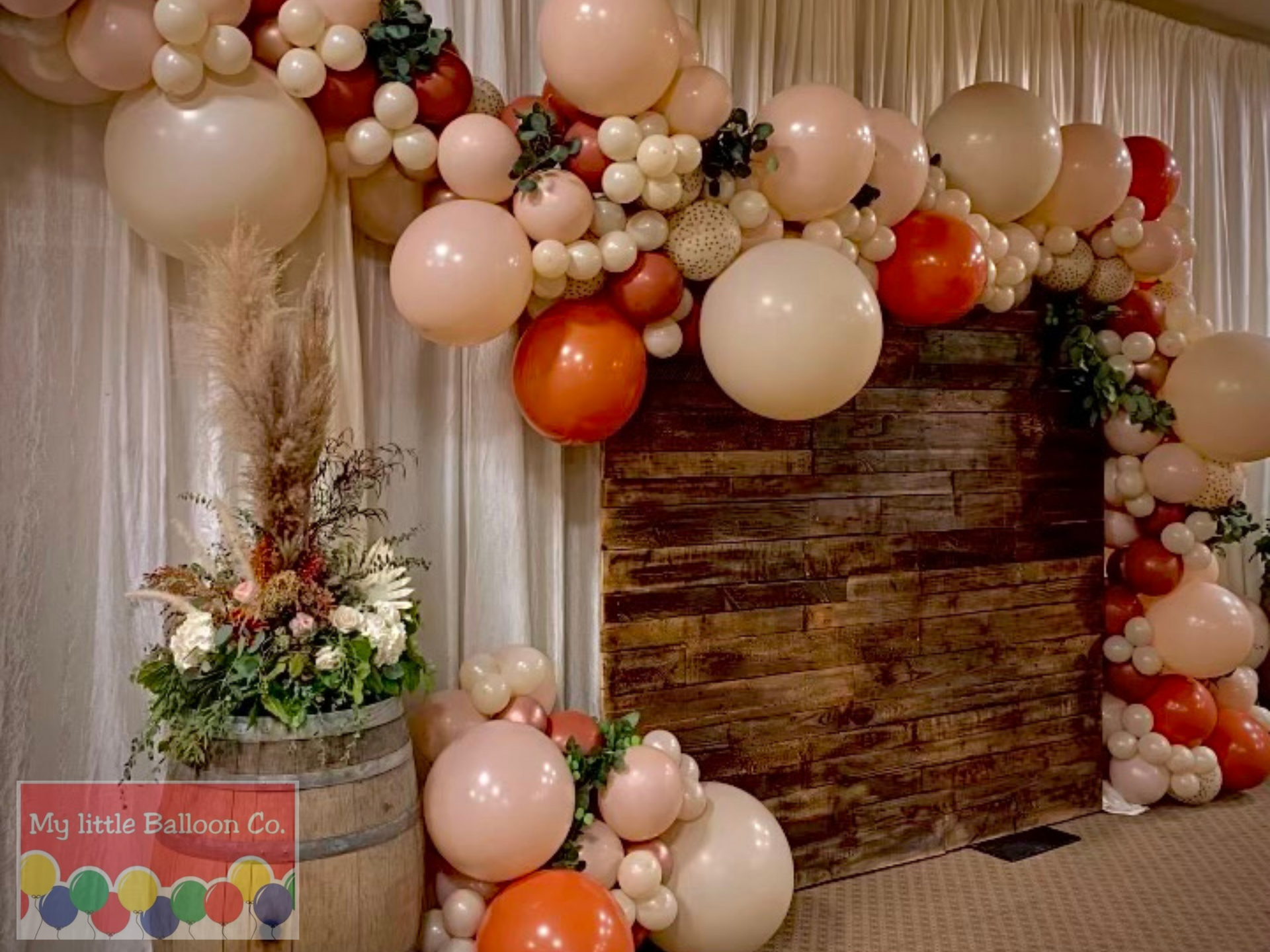 Balloon arch with wood backdrop; blush, peach, white, and brown balloons.