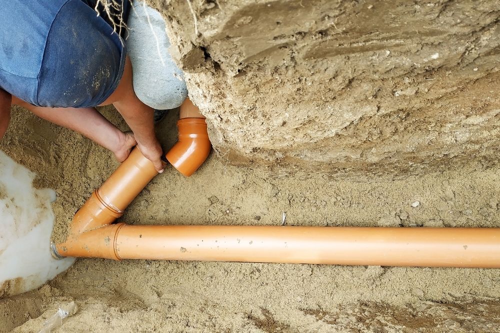 Person connecting orange PVC pipes in a trench.