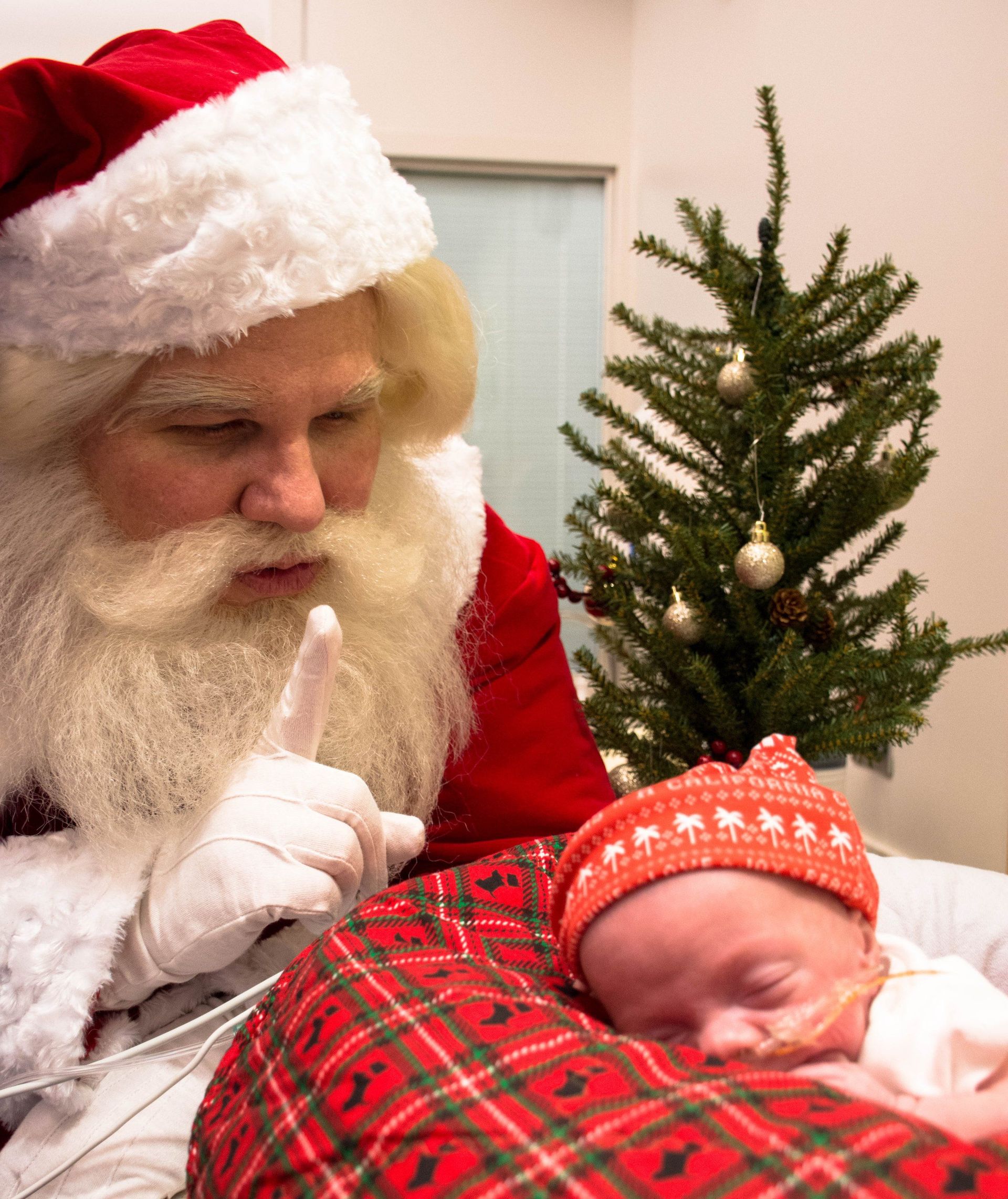 Santa claus is holding a baby in front of a christmas tree