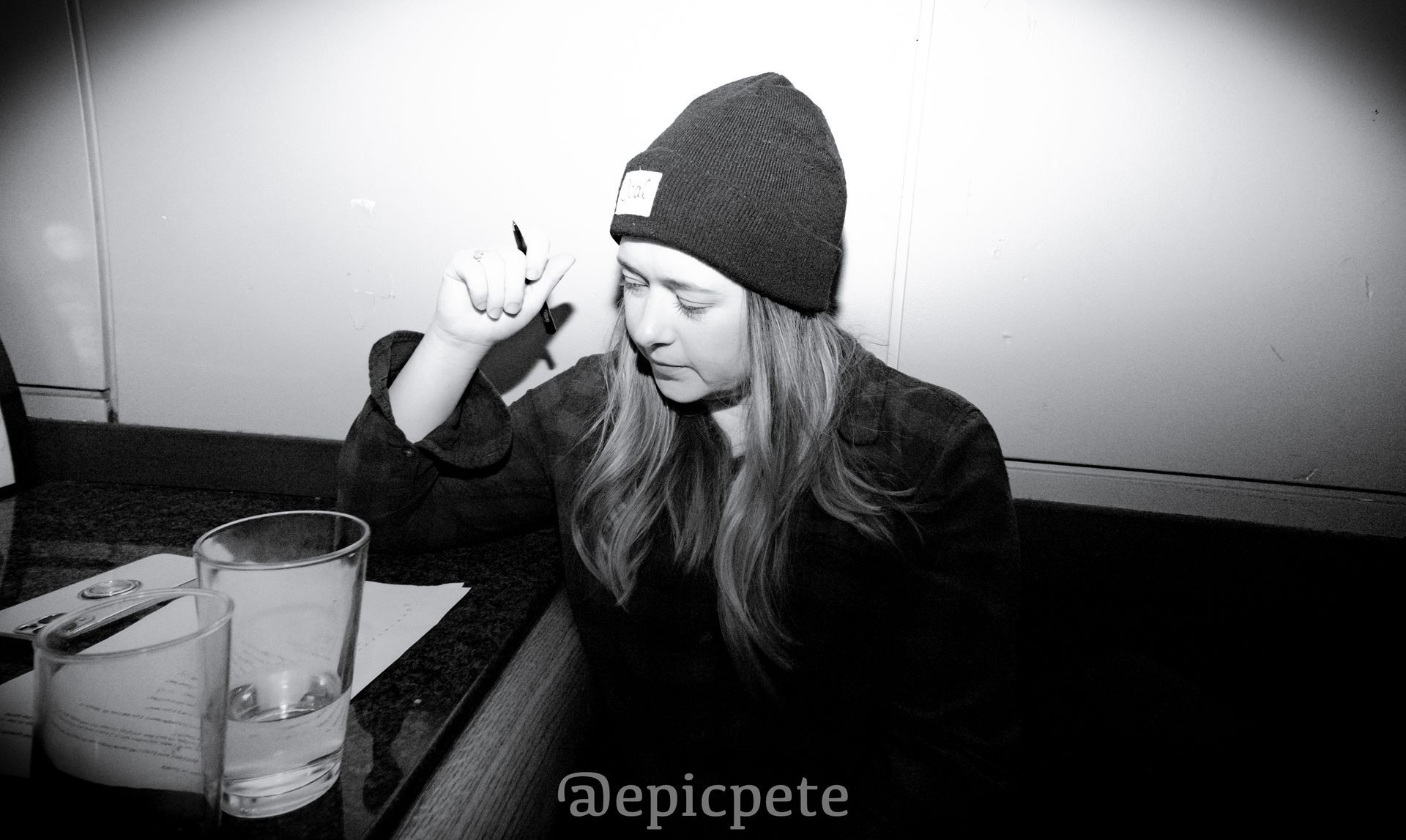 A woman in a beanie sits at a table with a glass of water