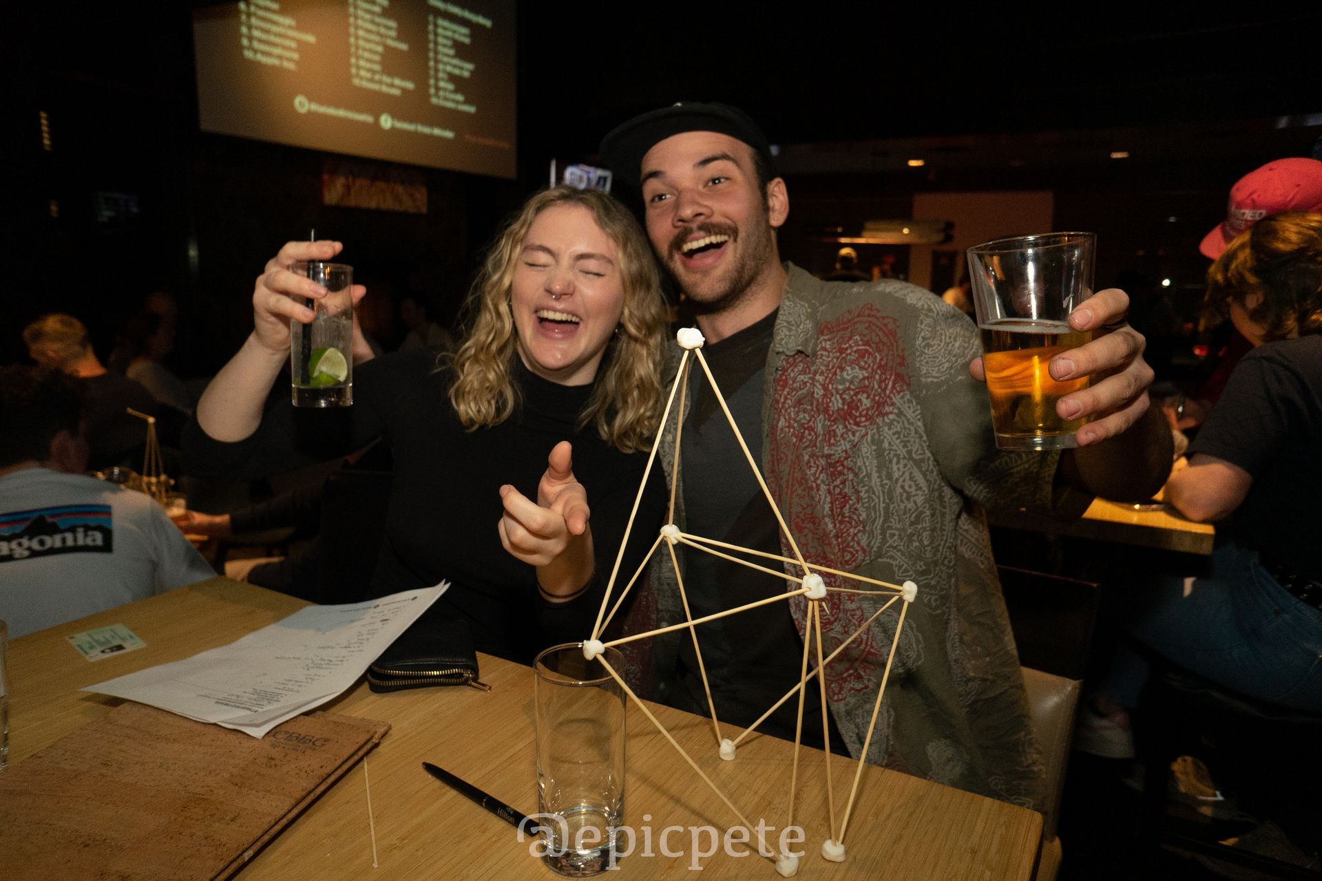 A man and a woman are sitting at a table holding drinks.