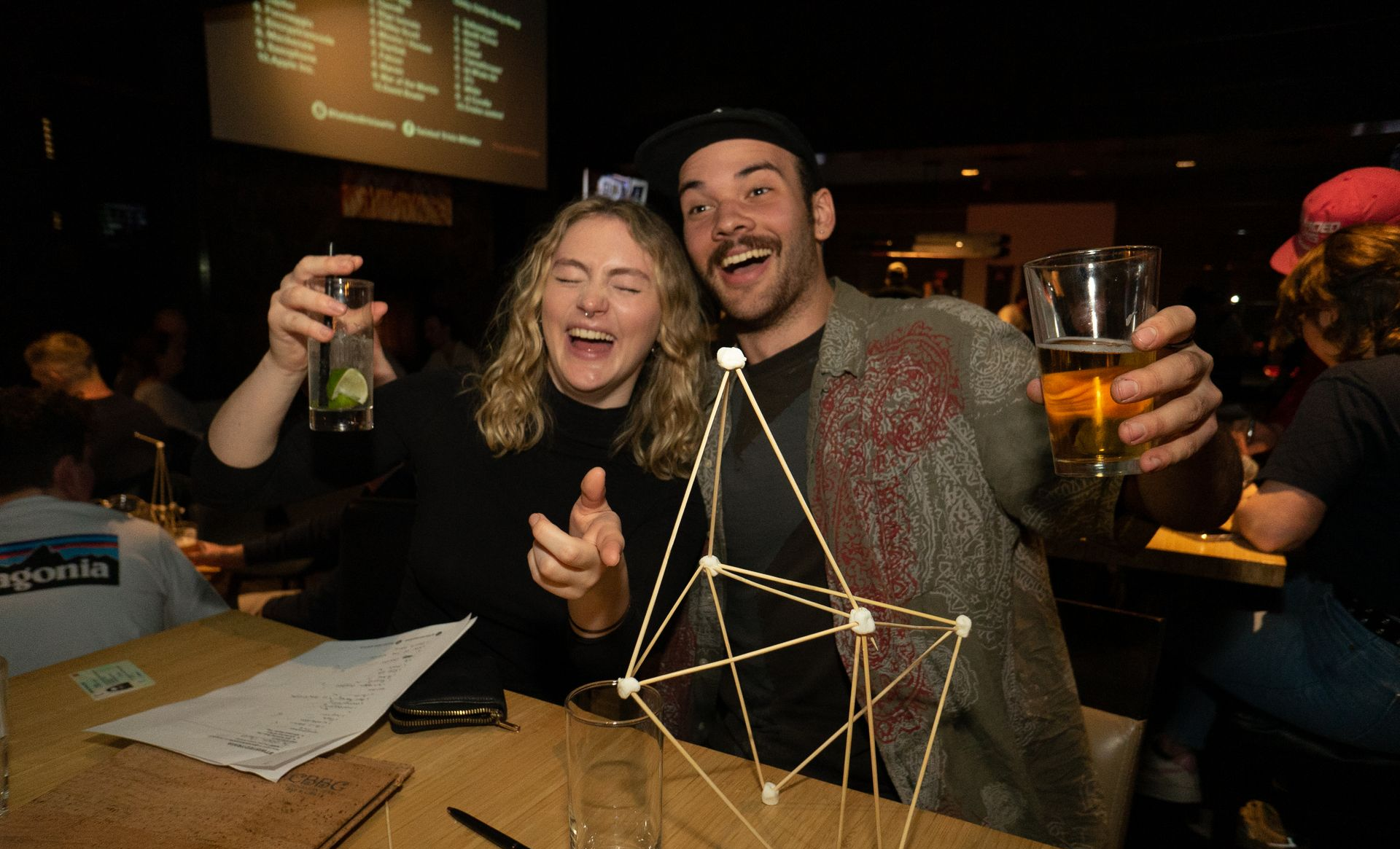 A man and a woman are sitting at a table holding drinks.