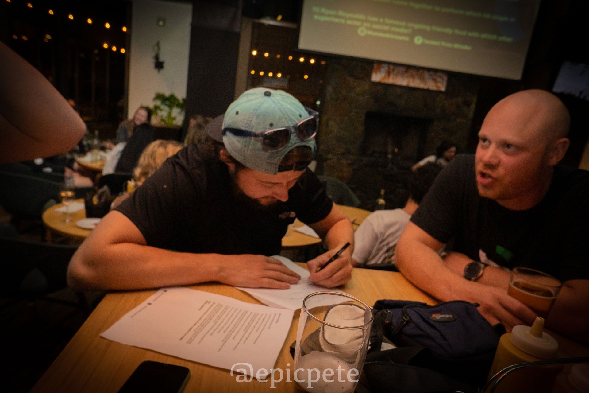 Two men are sitting at a table writing on a piece of paper.