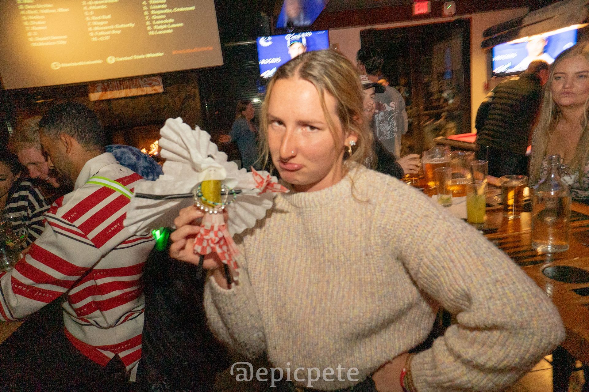 A woman in a sweater is holding a fan in a bar.