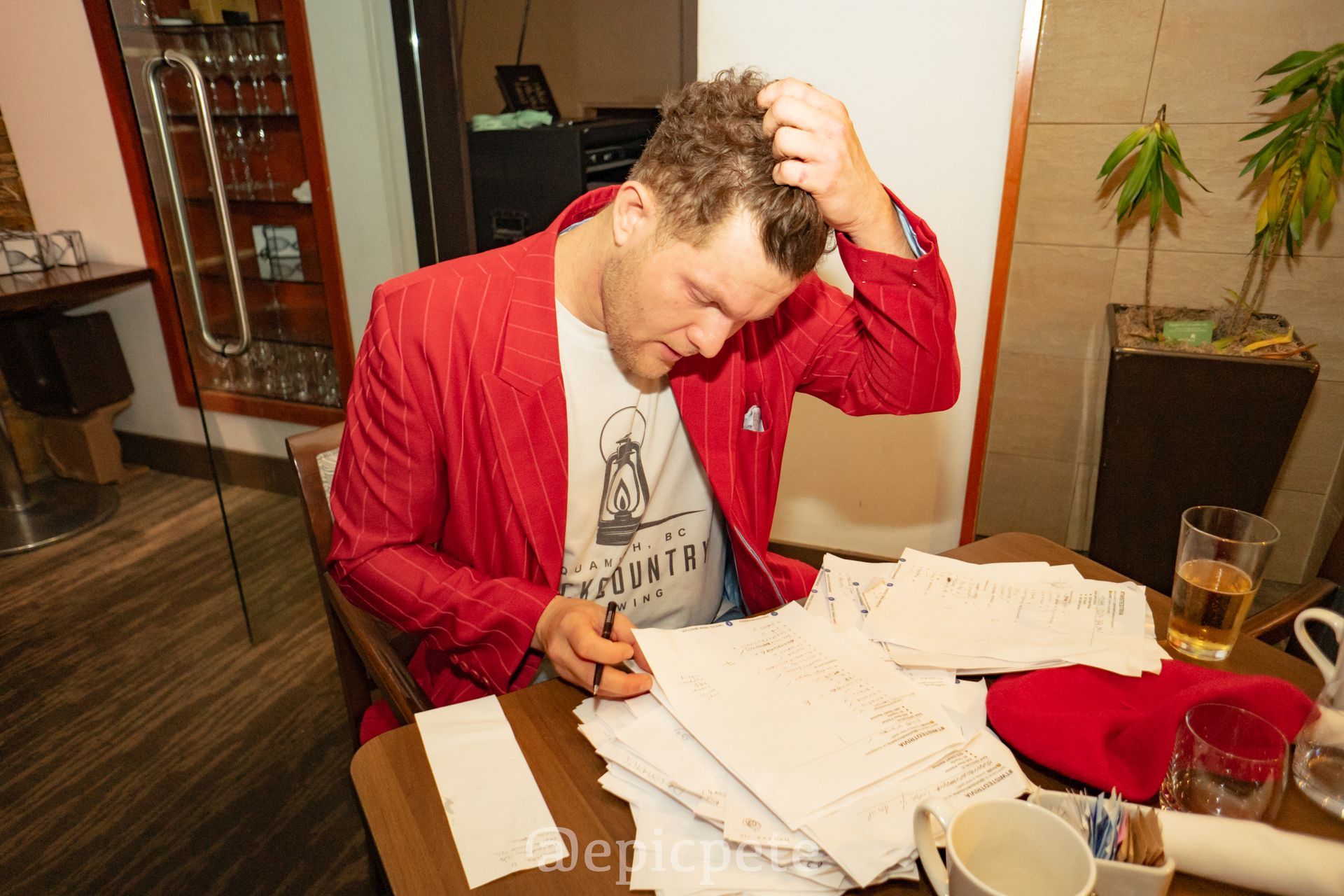 A man in a red suit is sitting at a table writing on a piece of paper.