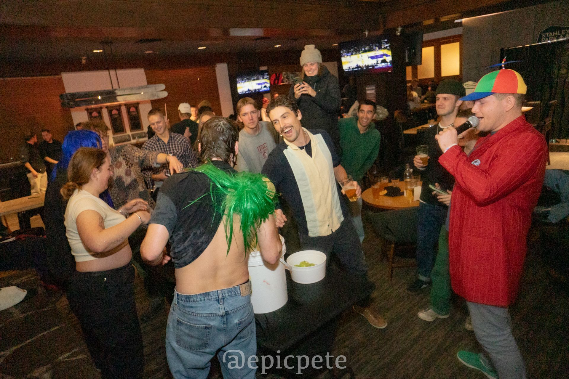 A group of people are dancing in a room and one of them has green hair.
