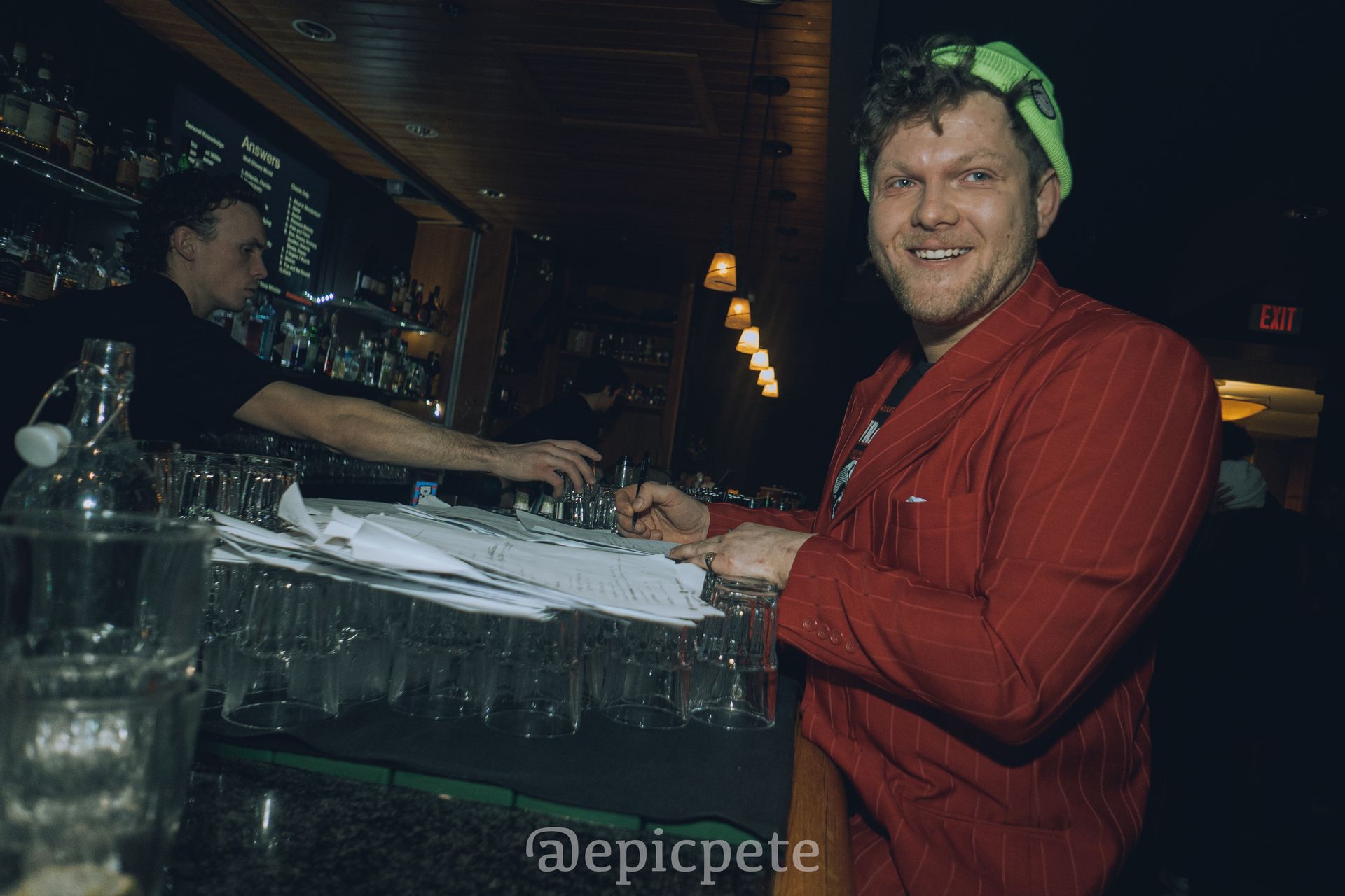 A man in a red jacket is standing behind a bar.
