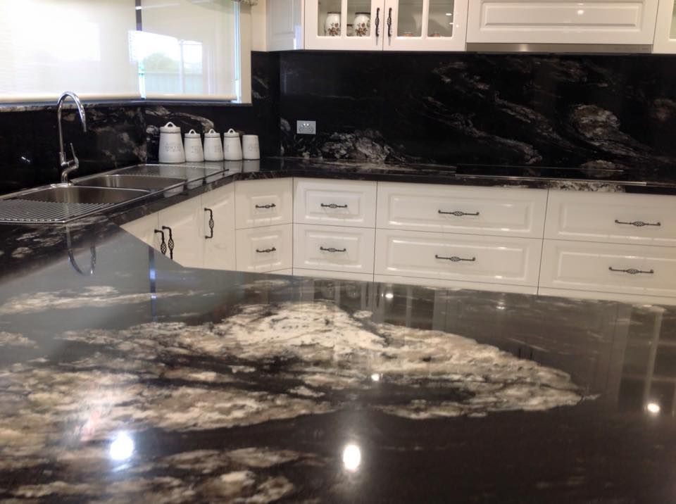 A kitchen with black granite counter tops and white cabinets.