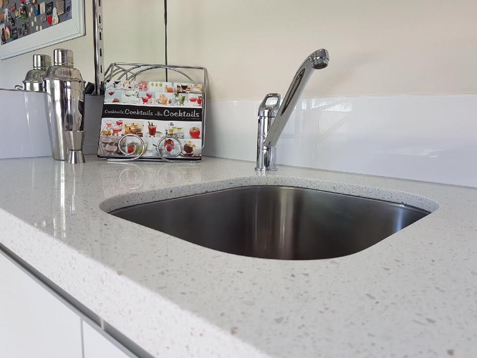 A stainless steel sink is on a white counter top in a kitchen.