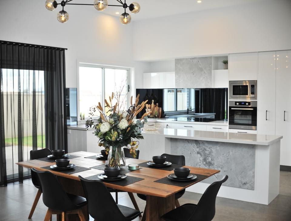 A dining room table and chairs in a kitchen with a vase of flowers on it.