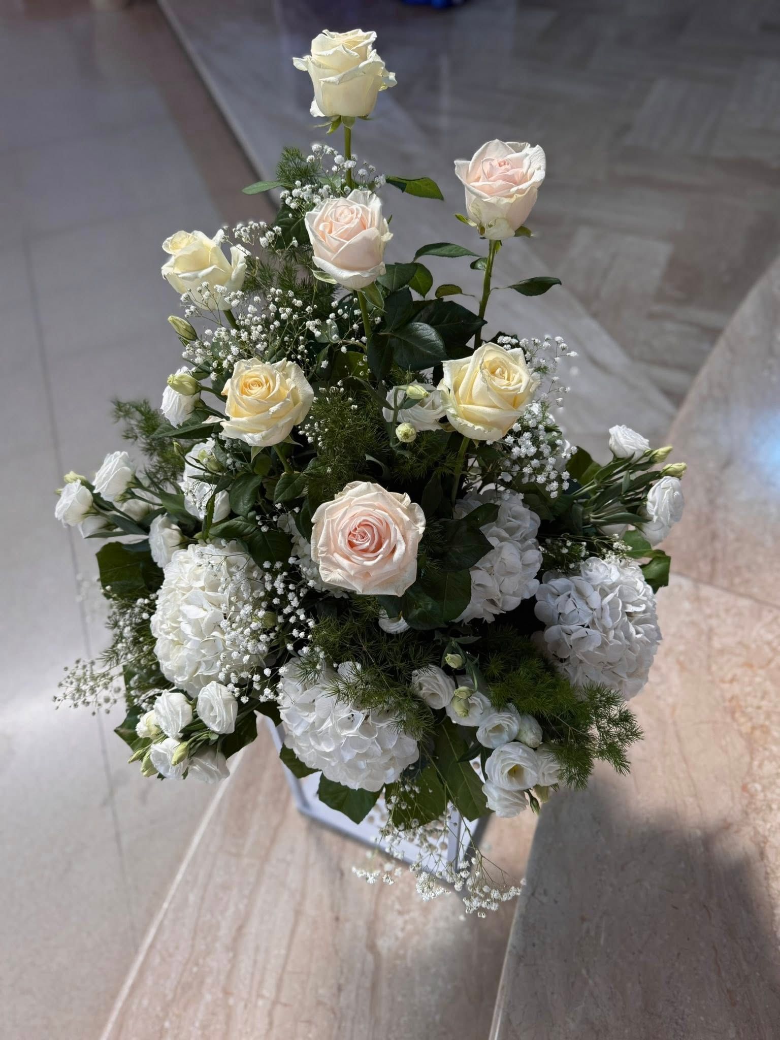 Composizione floreale in un contenitore quadrato; rose color crema e bianche, ortensie e gypsophila.