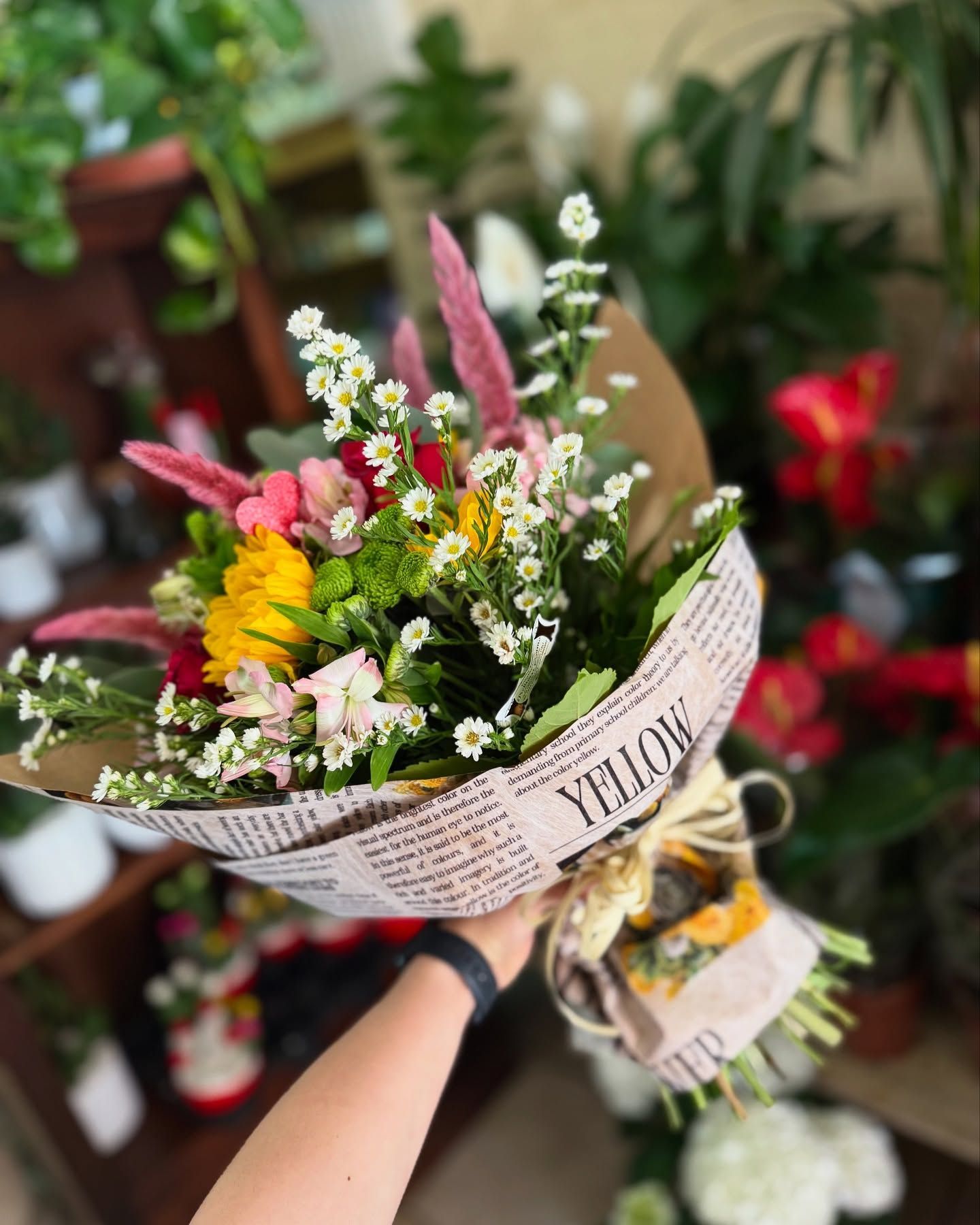 Mazzo di fiori colorati avvolto in carta tipo giornale, tenuto in mano da una persona.