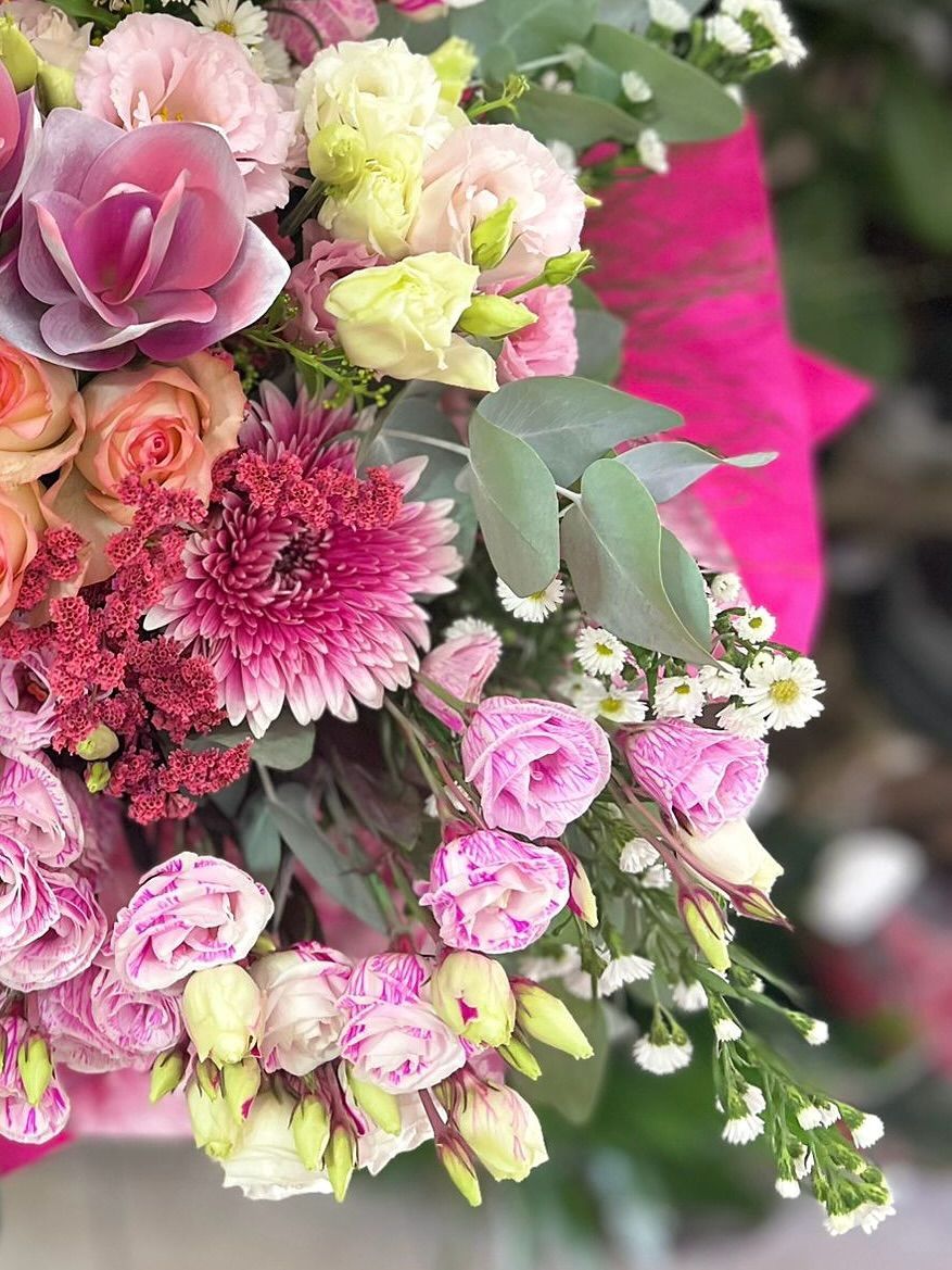 Primo piano di un bouquet con fiori rosa, pesca e bianchi, tra cui rose e lisianthus, su uno sfondo rosa.