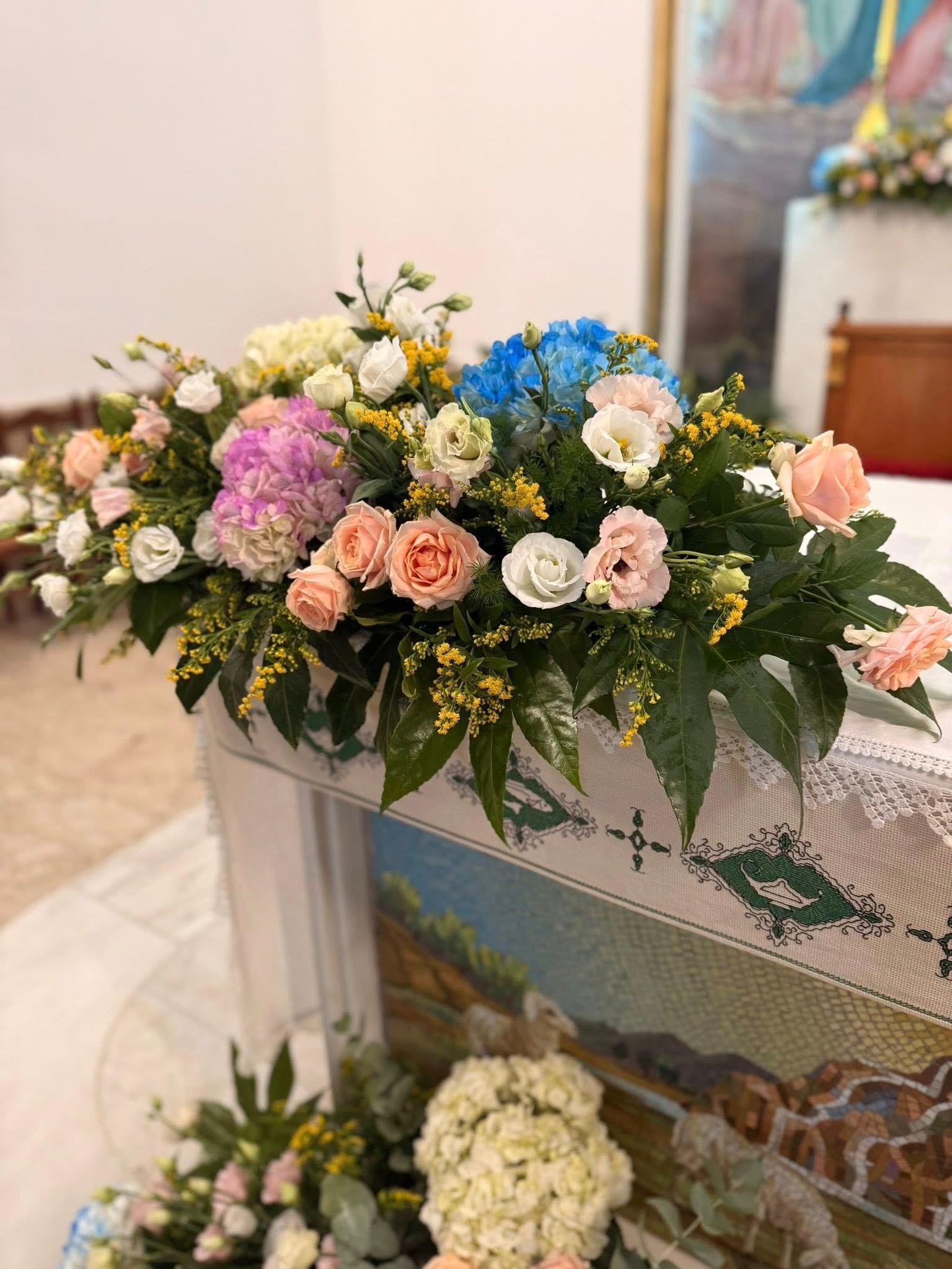 Composizione floreale di vari colori su un tavolo ricoperto di mosaico in una chiesa.