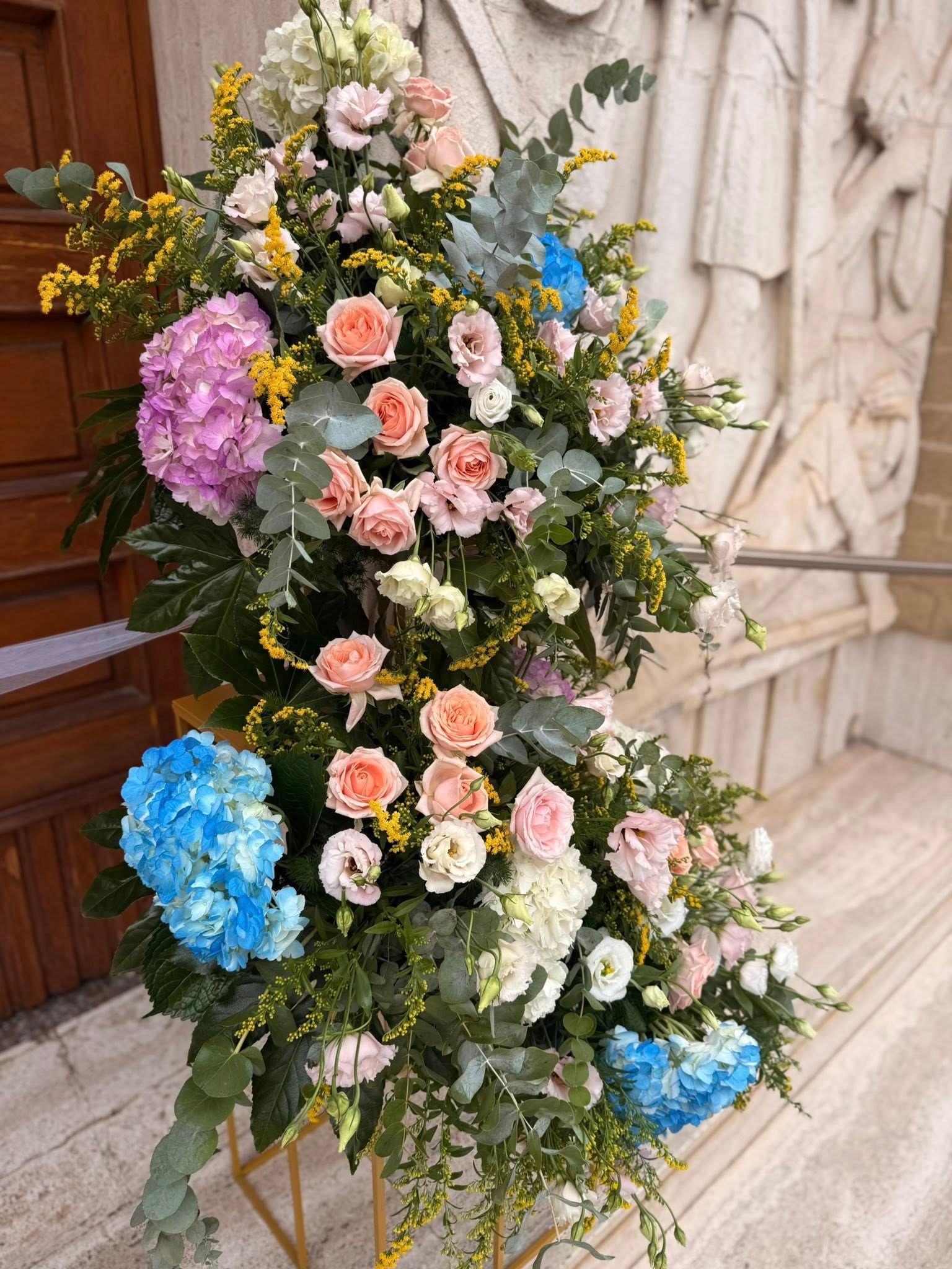 Grande composizione floreale con ortensie e rose in colori pastello, vicino a un edificio.